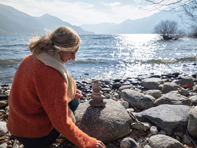 Mujer apilando piedras a la orilla de un lago