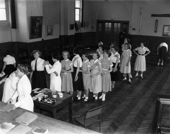7 de julio de 1955: Colegialas hacen cola para vacunarse contra la tuberculosis, durante una vacunación masiva realizada en la escuela secundaria Kilmorie, Londres. (Foto de Edward Miller / Keystone / Getty Images).